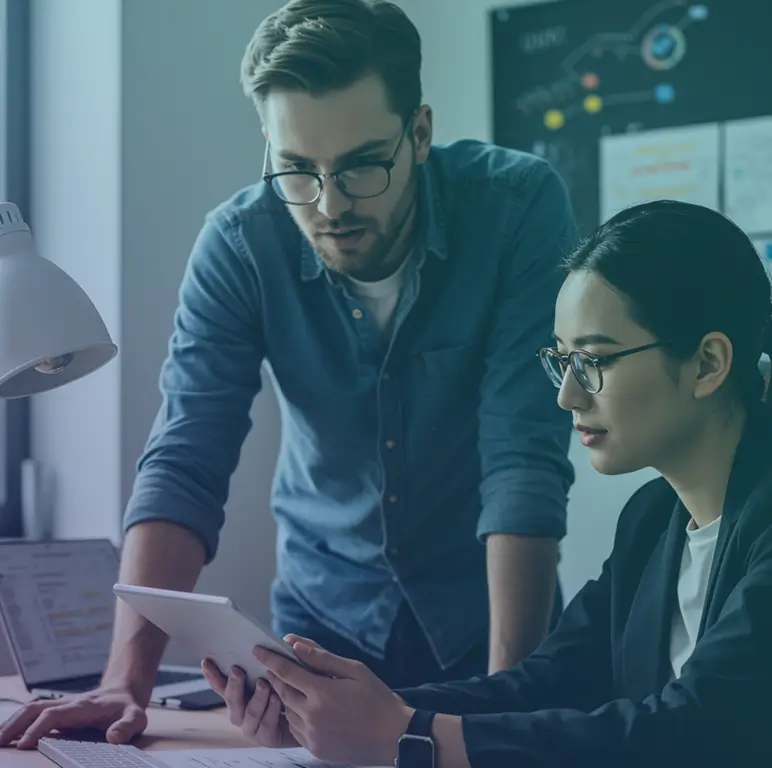 Two engineers collaborating over a tablet in a focused office environment, reviewing technical work together.